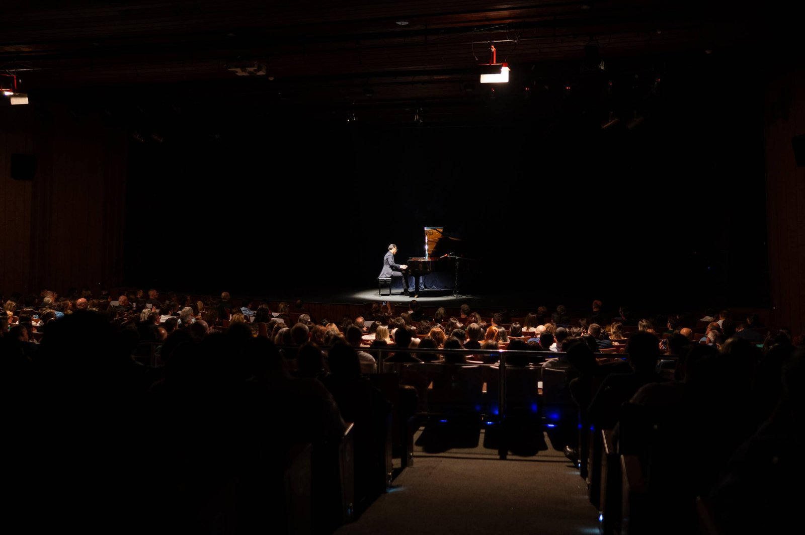 Alvaro Siviero ao piano, sozinho sob a luz do palco, diante de uma plateia lotada